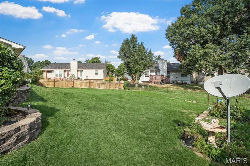 Expansive backyard with a manicured lawn, stone retaining wall, and mature trees — 355 Birmingham Drive, O'Fallon, MO 63366