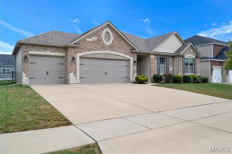 Brick and siding exterior featuring an arched entryway, two-car garage, and established front landscaping — 332 Mystic Brook Drive, O'Fallon, MO 63366