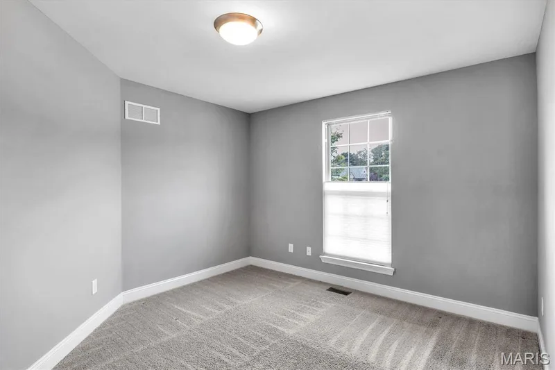 Neutral wall paint, textured carpet, window with white trim, white baseboards, and a flush-mount ceiling light — 332 Mystic Brook Drive, O'Fallon, MO 63366