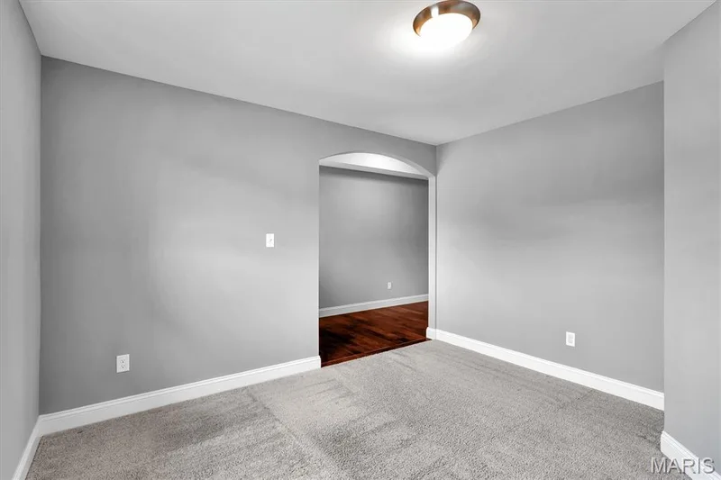 Light gray wall paint with white trim, gray carpet, flush-mount ceiling light, and an arched doorway — 332 Mystic Brook Drive, O'Fallon, MO 63366