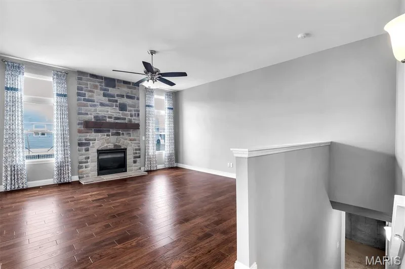 Spacious living area featuring rich wood-finish flooring and a stone-clad fireplace with a wood mantle — 332 Mystic Brook Drive, O'Fallon, MO 63366