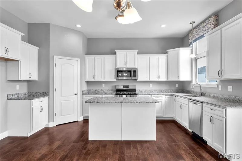 Kitchen featuring white cabinetry, light-toned countertops, a central island, wood-finish flooring, and stainless steel appliances — 332 Mystic Brook Drive, O'Fallon, MO 63366