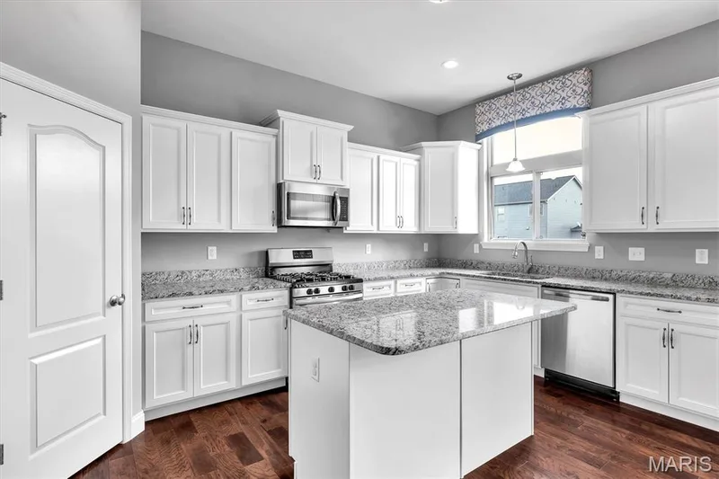 White cabinetry, stainless steel appliances, granite countertops, kitchen island, and wood-finish flooring — 332 Mystic Brook Drive, O'Fallon, MO 63366