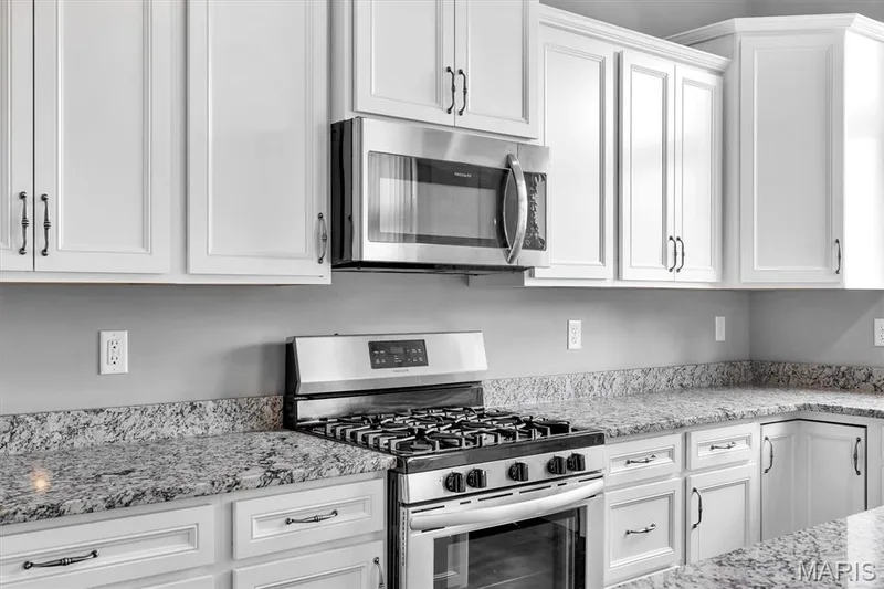 White shaker cabinetry with dark hardware, stainless steel gas range, over-the-range microwave, and light-toned speckled countertops — 332 Mystic Brook Drive, O'Fallon, MO 63366