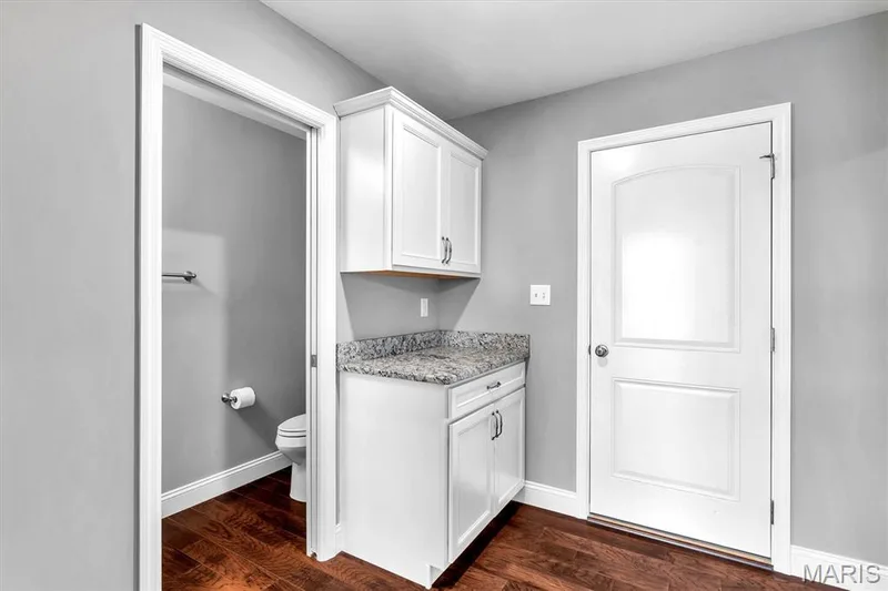 White cabinetry with dark hardware, stone countertop, wood-finish flooring, and light gray wall paint — 332 Mystic Brook Drive, O'Fallon, MO 63366