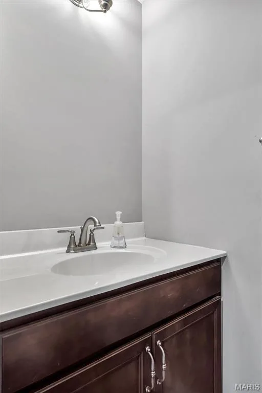 Vanity featuring a white countertop with an integrated sink, brushed nickel faucet, and dark wood-finish cabinetry with silver-tone hardware — 332 Mystic Brook Drive, O'Fallon, MO 63366