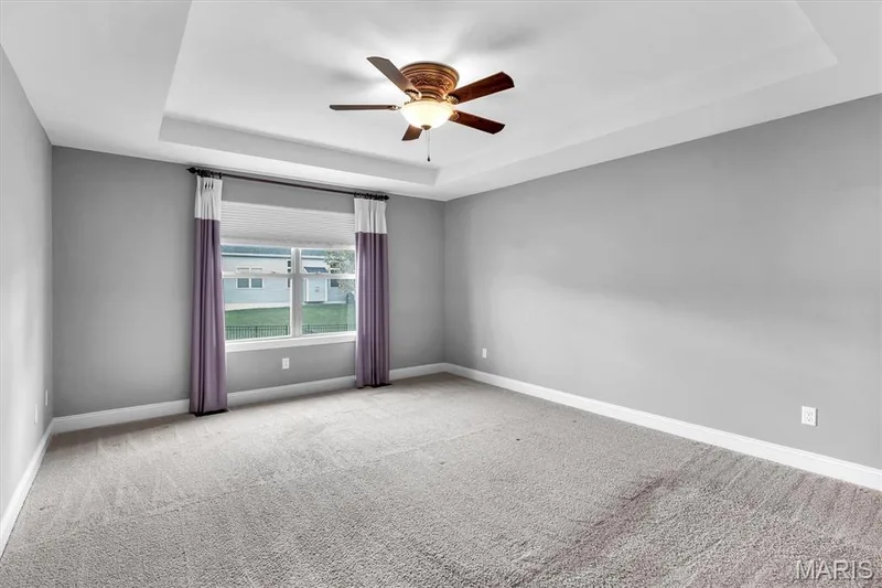 Tray ceiling with a decorative ceiling fan, light gray wall finish, and a window with white trim — 332 Mystic Brook Drive, O'Fallon, MO 63366
