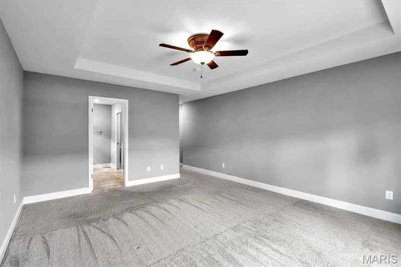 Tray ceiling with a decorative ceiling fan, light gray wall paint, and gray carpeting — 332 Mystic Brook Drive, O'Fallon, MO 63366
