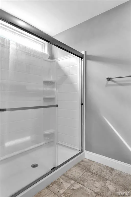 Shower enclosure with a clear glass sliding door, textured tile-patterned shower surround, integrated corner shelving, and a window for natural illumination — 332 Mystic Brook Drive, O'Fallon, MO 63366