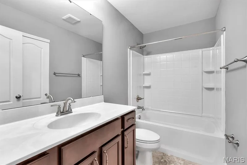 Vanity with integrated sink, brushed nickel faucet, large wall mirror, wood-finish cabinetry, and a tub with a shower surround — 332 Mystic Brook Drive, O'Fallon, MO 63366