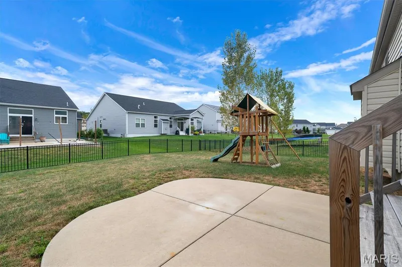 Expansive backyard featuring a concrete patio, wood deck, black metal fencing, and a wooden play structure — 332 Mystic Brook Drive, O'Fallon, MO 63366
