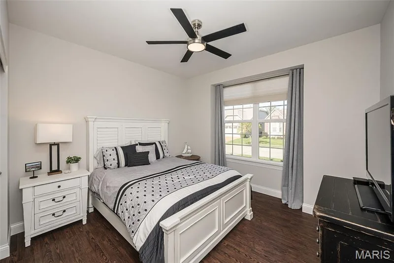 Wood-finish flooring, white paneled headboard, ceiling fan with brushed nickel hardware, window with grid pattern, and neutral wall paint — 1509 Woodside Hills Drive, St Peters, MO 63376