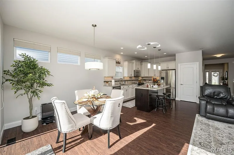 Open-concept living area with wood-finish flooring, a kitchen island with seating, pendant lighting, recessed lighting, and white cabinetry — 1509 Woodside Hills Drive, St Peters, MO 63376