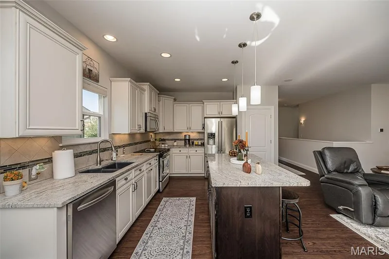 Kitchen featuring white cabinetry, stainless steel appliances, a multi-tone tile backsplash, and an island with a light-toned countertop — 1509 Woodside Hills Drive, St Peters, MO 63376