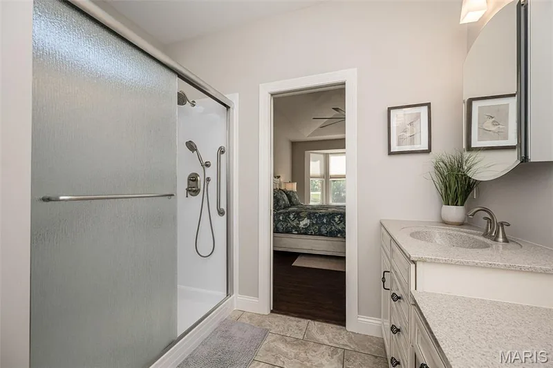 Frosted glass shower enclosure with grab bar, vanity with stone-finish countertop, single basin sink, and brushed nickel fixtures — 1509 Woodside Hills Drive, St Peters, MO 63376
