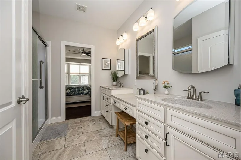 Dual vanity with light-colored countertops, white cabinetry with dark hardware, and a tiled shower with a glass enclosure — 1509 Woodside Hills Drive, St Peters, MO 63376