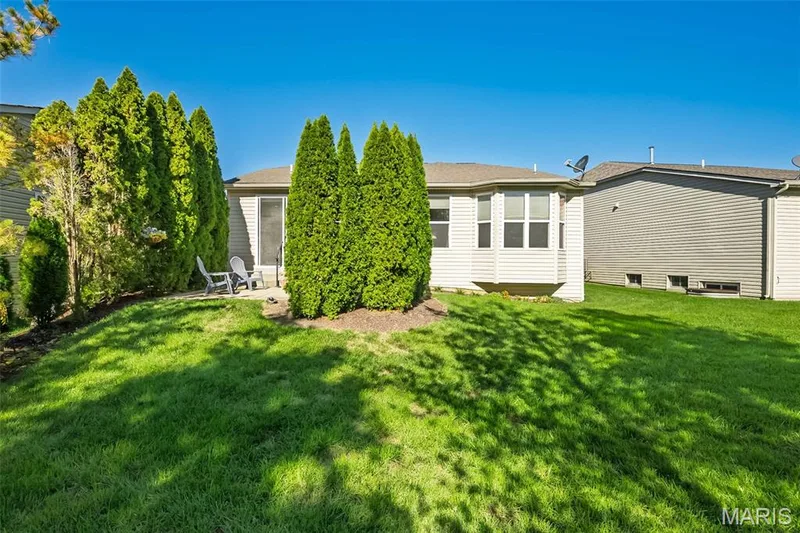 Expansive green lawn with mature evergreen trees and a paved patio area — 1509 Woodside Hills Drive, St Peters, MO 63376