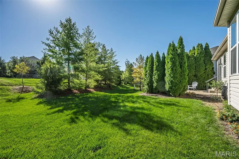 Expansive manicured lawn with mature trees, established evergreen landscaping, and a side patio area — 1509 Woodside Hills Drive, St Peters, MO 63376