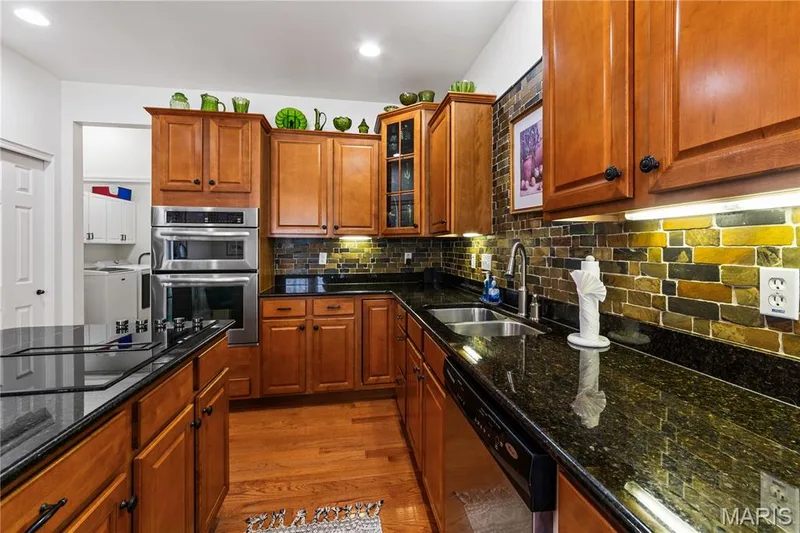 Kitchen featuring wood cabinetry, stainless steel appliances, dark granite countertops, and a multicolor tile backsplash — 149 Amiot Court, Chesterfield, MO 63146