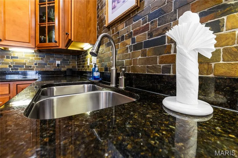 Dual stainless steel undermount sink with a brushed nickel gooseneck faucet, dark speckled countertops, and a multi-toned brick-patterned tile backsplash — 149 Amiot Court, Chesterfield, MO 63146