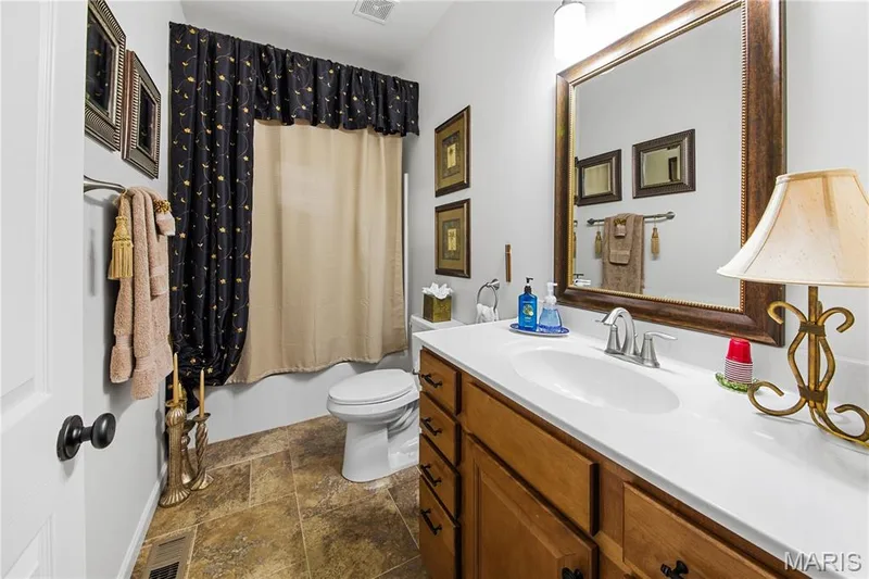 Warm-toned tile flooring, wood-finish vanity with drawer storage, integrated sink, and a large framed mirror — 149 Amiot Court, Chesterfield, MO 63146