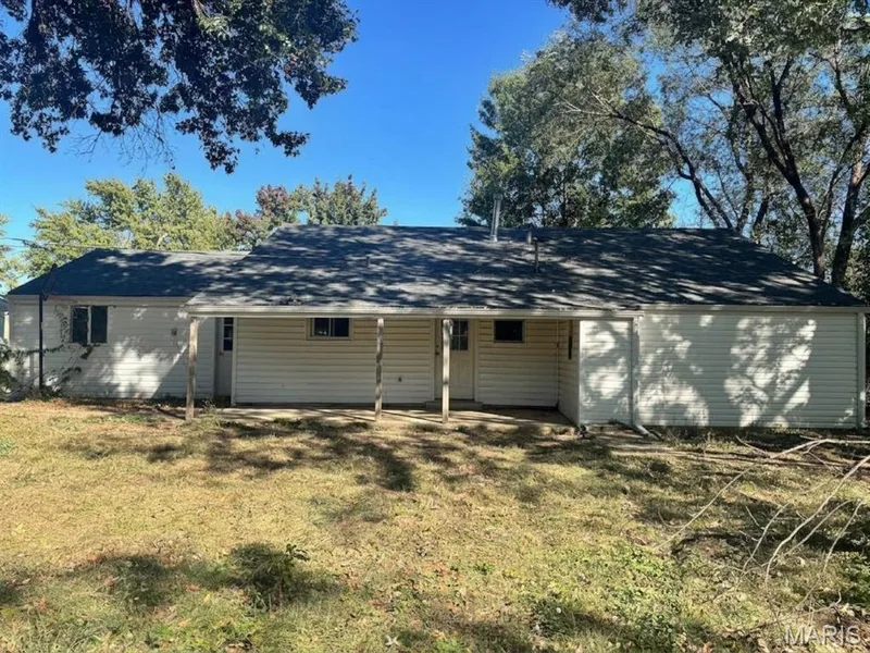 Single-story residence featuring light-colored horizontal siding, a gabled roof, and a covered patio supported by structural columns — 204 Allen Drive, O'Fallon, MO 63366