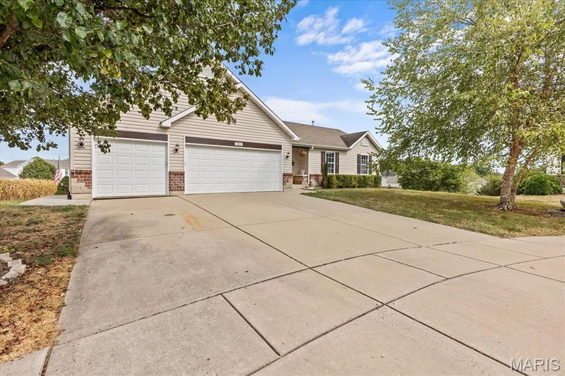 Exterior featuring light-colored siding, brick accents, a two-car garage, and a concrete driveway — 521 Cimarron Woods Court, Wentzville, MO 63385