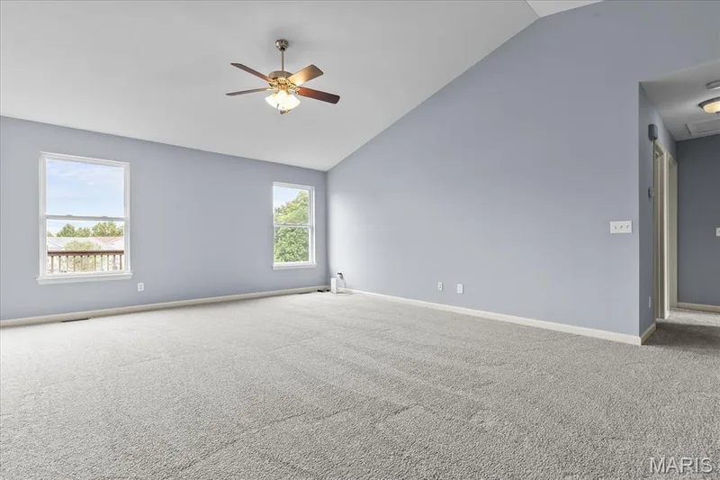 Expansive room with vaulted ceilings, two large windows, a ceiling fan with integrated lighting, and plush carpeting — 521 Cimarron Woods Court, Wentzville, MO 63385