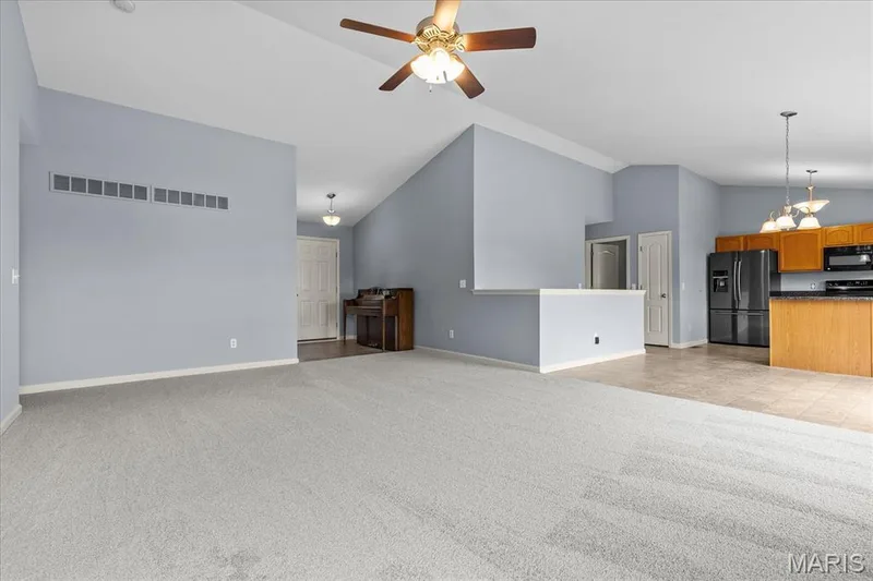 Vaulted ceiling with a ceiling fan, light-toned carpeting, and a kitchen featuring wood-finish cabinetry, black appliances, and dark countertops — 521 Cimarron Woods Court, Wentzville, MO 63385