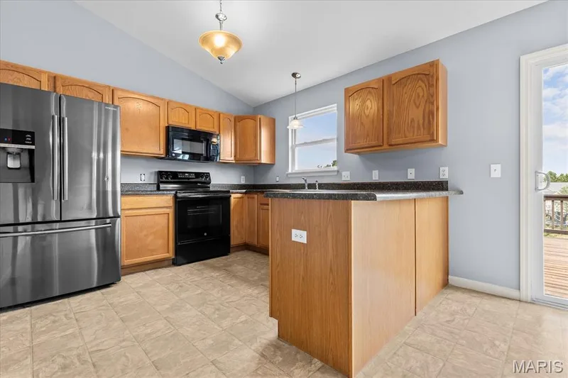 Kitchen featuring wood cabinetry, stainless steel refrigerator, black range, black microwave, and dark countertops — 521 Cimarron Woods Court, Wentzville, MO 63385