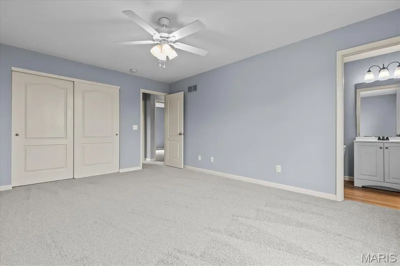 Spacious room featuring light-colored carpeting, a ceiling fan with integrated lighting, and a doorway leading to a bathroom with a vanity and mirror — 521 Cimarron Woods Court, Wentzville, MO 63385
