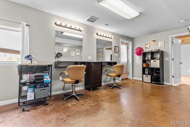 Expansive room featuring two vanity stations with built-in mirrors and overhead lighting, brown-toned flooring, and a window with white window treatments — 521 Cimarron Woods Court, Wentzville, MO 63385