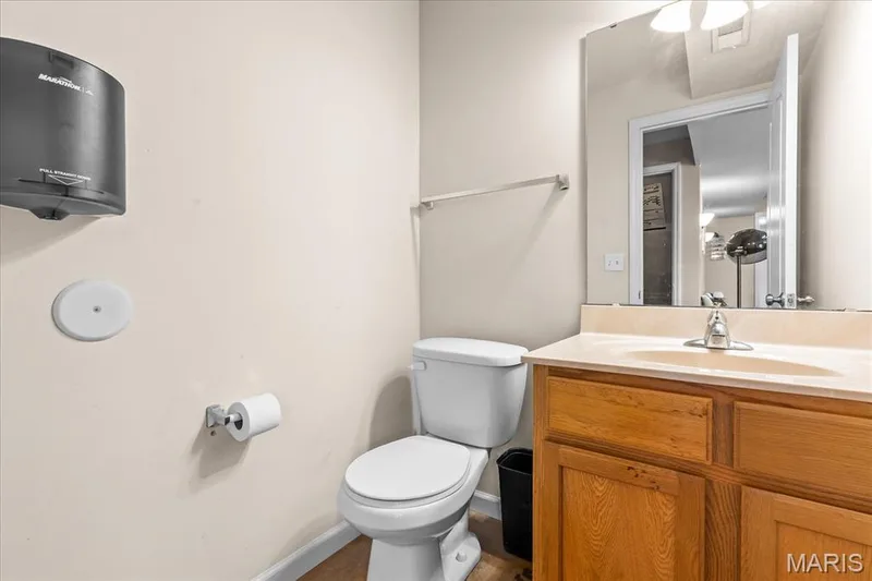 Bathroom featuring a vanity with a light wood-finish cabinet and an integrated sink, a wall-mounted mirror, and a toilet — 521 Cimarron Woods Court, Wentzville, MO 63385