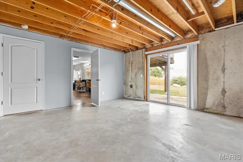Exposed wood ceiling beams, concrete flooring, sliding glass door, white interior doors, and a partial finished wall with a painted surface — 521 Cimarron Woods Court, Wentzville, MO 63385