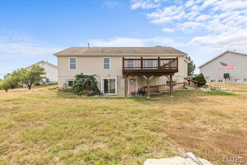 Expansive rear yard with a two-story residence featuring siding, a raised deck, and a walk-out lower level with a sliding glass door — 521 Cimarron Woods Court, Wentzville, MO 63385