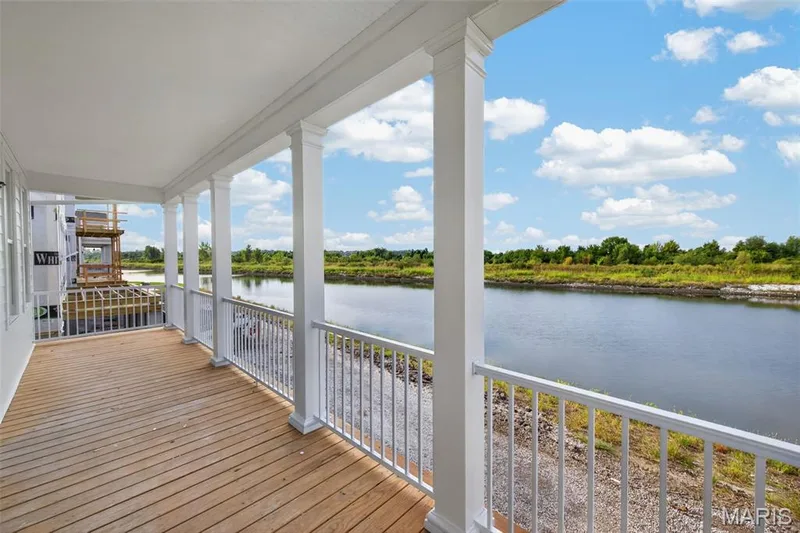 Expansive outdoor balcony featuring wood-finish decking, white railings, and white columns overlooking a natural waterway and distant greenery — 2974 Memphis Street, St Charles, MO 63301