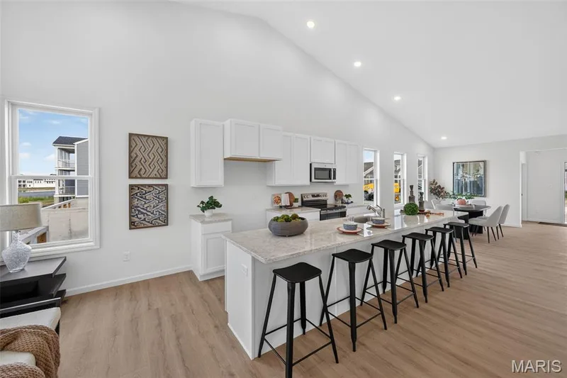 Open-concept living space featuring vaulted ceilings, LVP flooring, a kitchen island with seating, white cabinetry, and stainless steel appliances — 2974 Memphis Street, St Charles, MO 63301