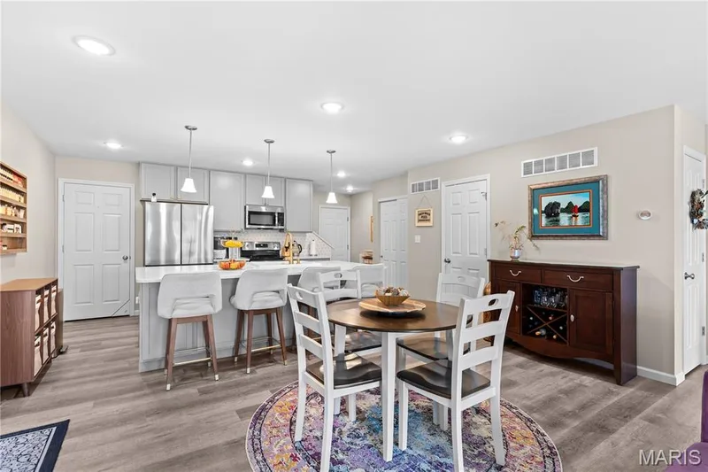 Open-concept kitchen and dining area featuring light gray cabinetry, stainless steel appliances, a center island with countertop seating, and recessed lighting — 200 Tiber Way, St Charles, MO 63301