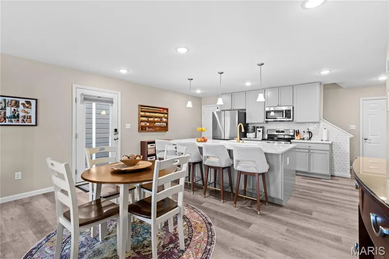 Contemporary kitchen featuring light gray cabinetry, stainless steel appliances, a large island with seating, and luxury vinyl plank flooring — 200 Tiber Way, St Charles, MO 63301