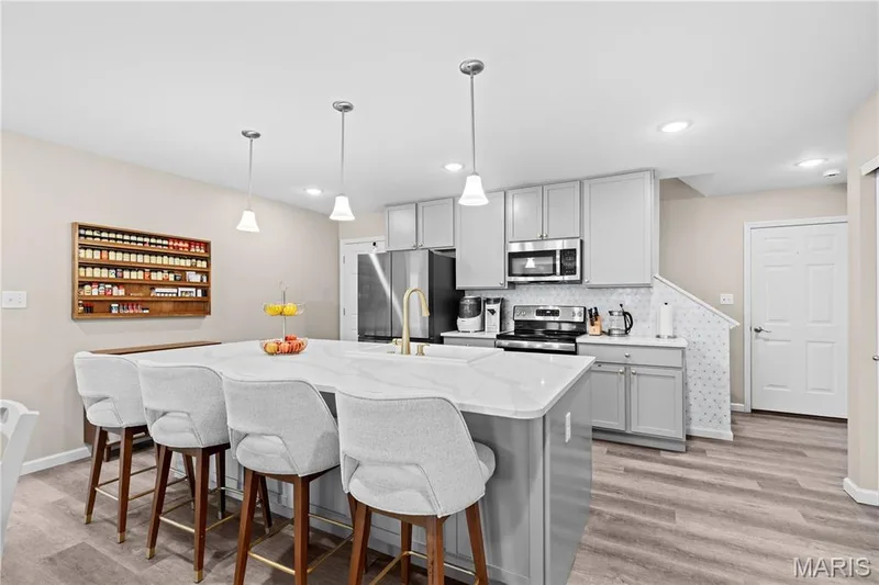 Spacious kitchen with a central island, light gray cabinetry, stainless steel appliances, and luxury vinyl plank flooring — 200 Tiber Way, St Charles, MO 63301