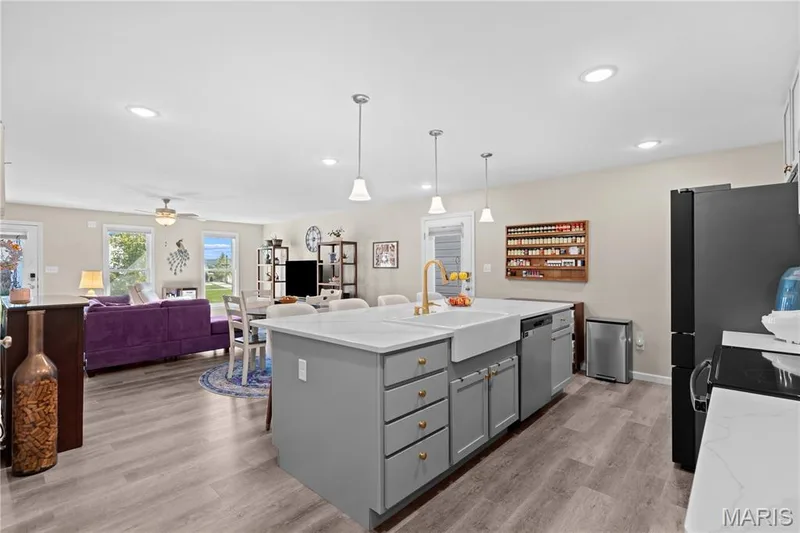 Open-concept kitchen with a large island, farm sink, pendant lighting, and luxury vinyl plank flooring — 200 Tiber Way, St Charles, MO 63301
