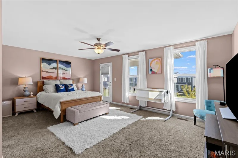 Light-hued walls, carpeted flooring, two windows with white trim, and a ceiling fan with integrated lighting, door leading to 2nd-story balcony deck overlooking the community green space — 200 Tiber Way, St Charles, MO 63301