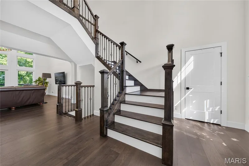 Grand staircase with dark wood-finish treads, white risers, and wrought iron balusters — 713 High Point Drive, Lake St. Louis, MO 63367