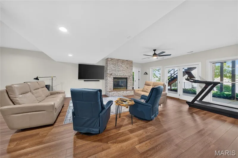 Spacious family room featuring wood laminate flooring, a brick-surround fireplace, a ceiling fan, and multiple glass doors opening to the exterior — 713 High Point Drive, Lake St. Louis, MO 63367