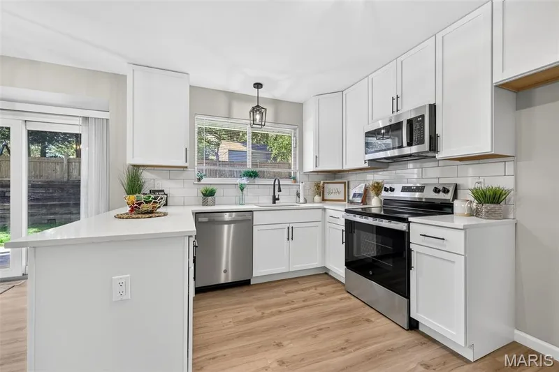 Kitchen featuring white cabinetry, stainless steel appliances, white subway tile backsplash, light wood-finish flooring, and a sliding glass door — 341 Westbrook Drive, O'Fallon, MO 63366