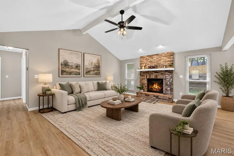 Vaulted ceiling with exposed beams, brick-faced fireplace with hearth, wood-finish flooring, ceiling fan with integrated lighting, and multiple windows — 341 Westbrook Drive, O'Fallon, MO 63366