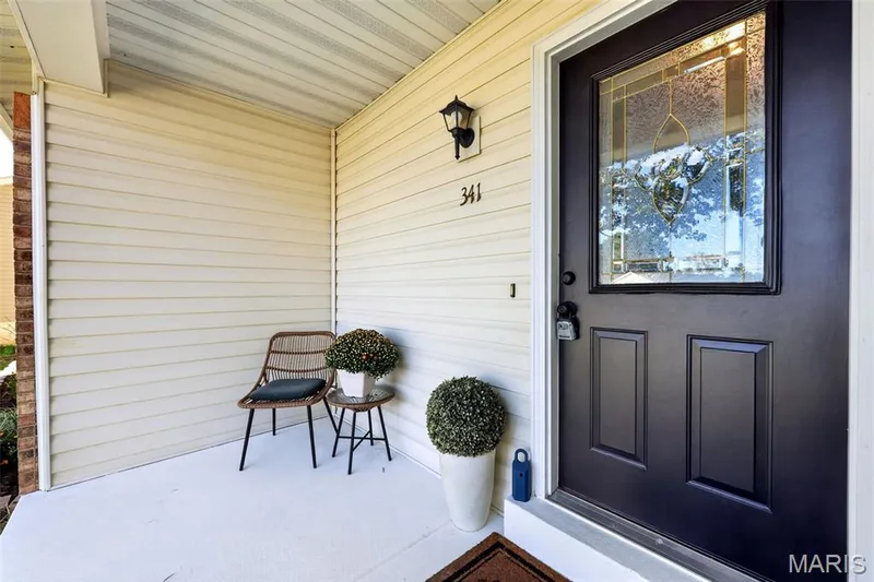 Front entryway featuring a black paneled door with decorative leaded glass, exterior wall sconce, and house numbers — 341 Westbrook Drive, O'Fallon, MO 63366