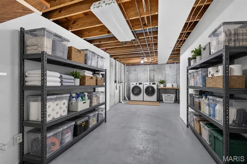 Painted concrete flooring, exposed wooden ceiling beams, dual laundry machines, metal shelving units, and a utility sink with a wood-finish countertop — 341 Westbrook Drive, O'Fallon, MO 63366
