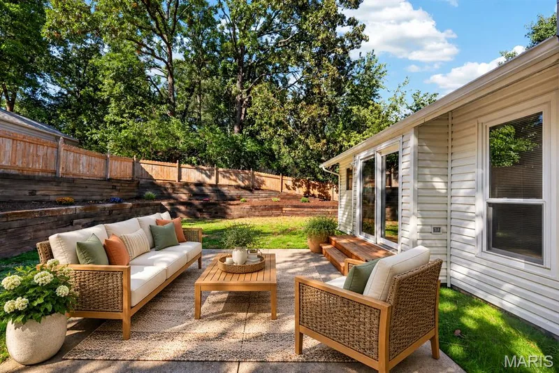 Concrete patio with a wood-finish fence, tiered landscaping, and mature trees — 341 Westbrook Drive, O'Fallon, MO 63366