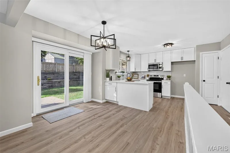 Wood-finish flooring, white cabinetry, stainless steel appliances, kitchen island with counter seating, and sliding glass doors to the exterior — 341 Westbrook Drive, O'Fallon, MO 63366
